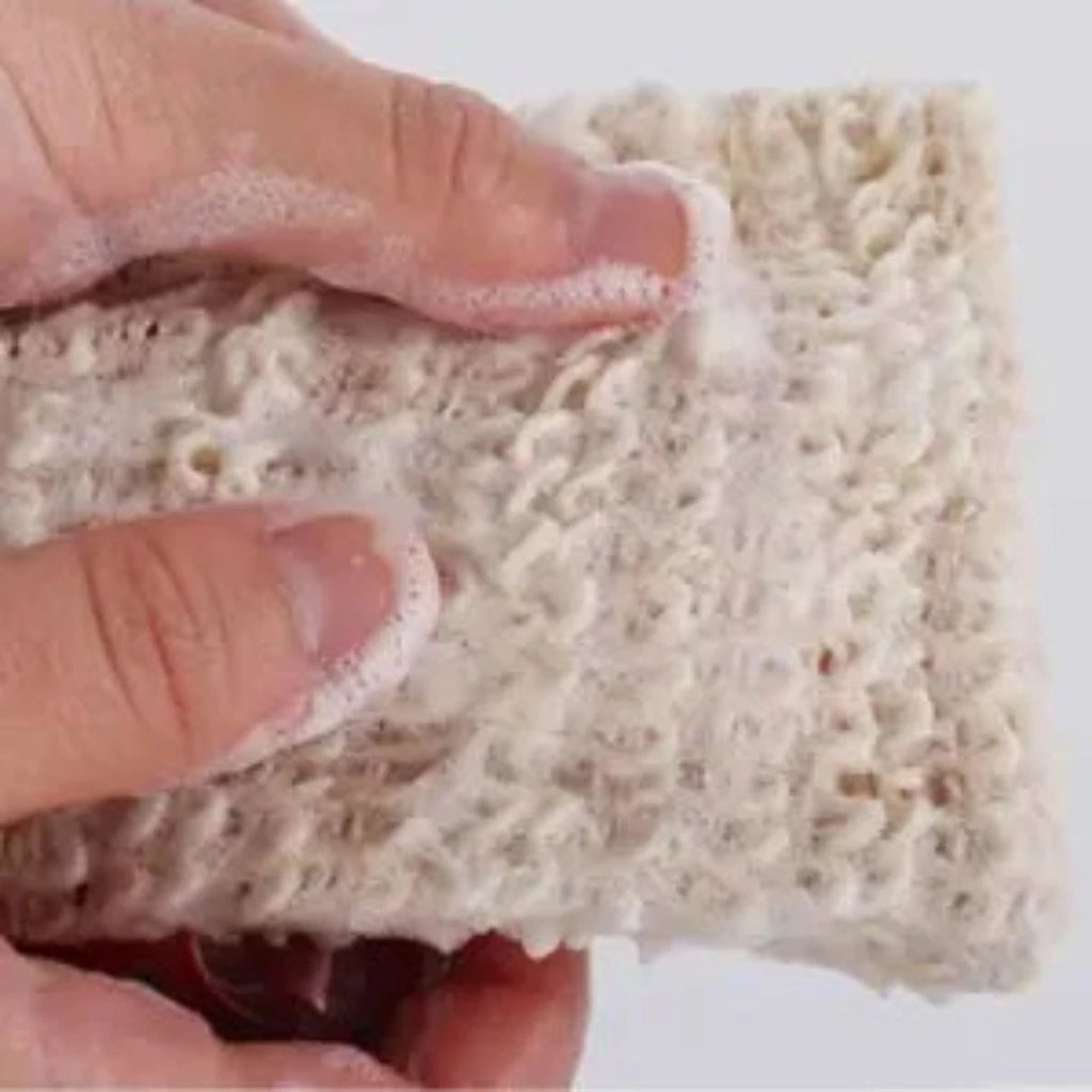 Close-up of a hand holding a lathered sisal mesh pouch, showing the open weave texture covered in soap foam